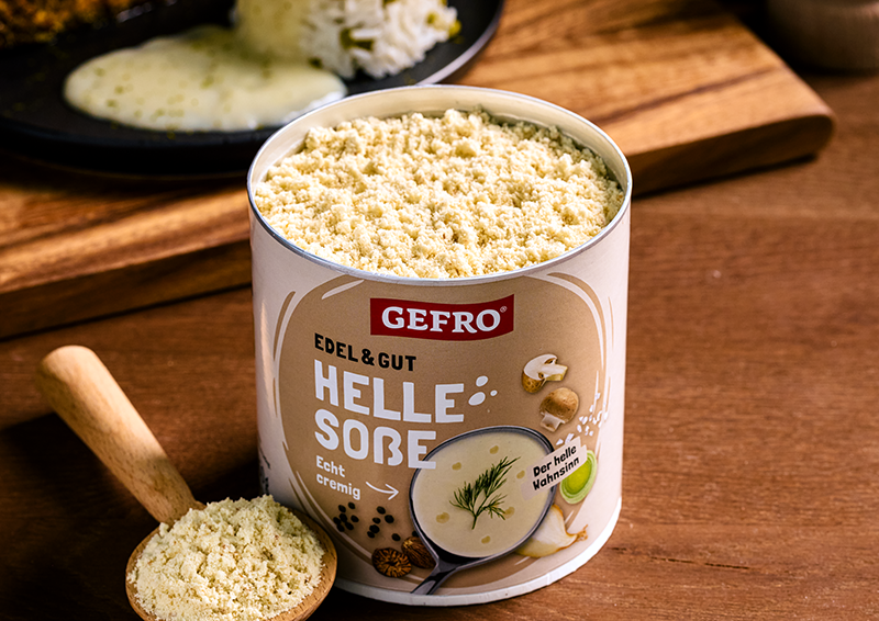 Dose GEFRO Helle Soße mit cremigem Soßenpulver auf Holztisch, daneben ein Holzlöffel mit Pulver.