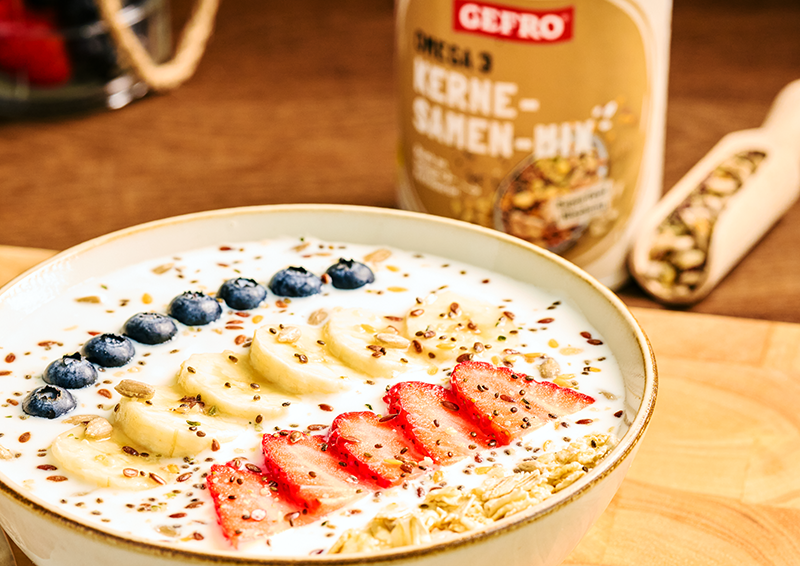 Schale mit Joghurt, Banane, Erdbeeren, Blaubeeren und Körnermix als gesundes Frühstück auf Holztisch
