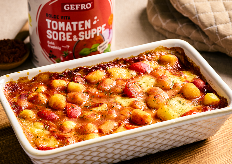 Auflauf mit Gnocchi, Tomatensoße und überbackenem Käse in weißer Form, dahinter ein Gefro-Produkt im Hintergrund