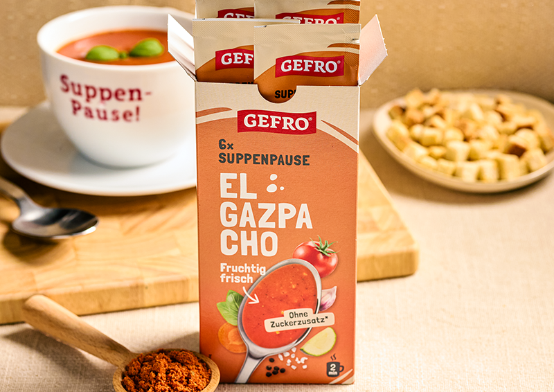 GEFRO El Gazpacho Suppenpause in geöffneter Packung, dazu eine Schale Suppe und Croutons im Hintergrund