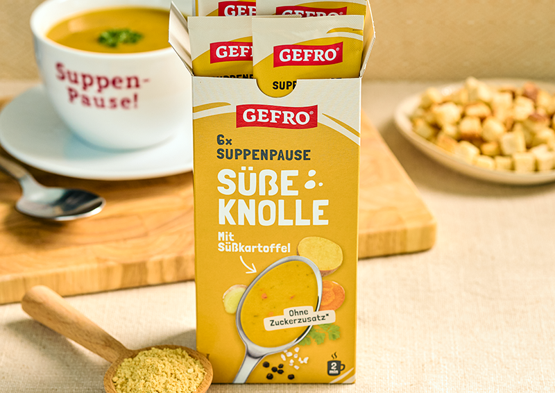 GEFRO Suppenpause Süße Knolle mit Süßkartoffel in der Packung, daneben Suppe in Tasse und Croutons im Hintergrund