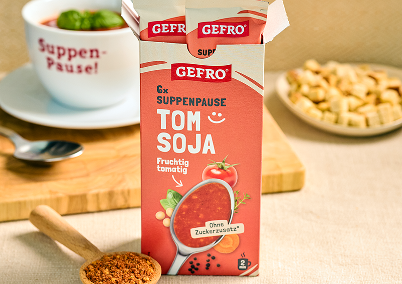 GEFRO Tom Soja Suppenpause in geöffneter Packung auf Tisch, daneben Tasse Suppe und Löffel mit Gewürz