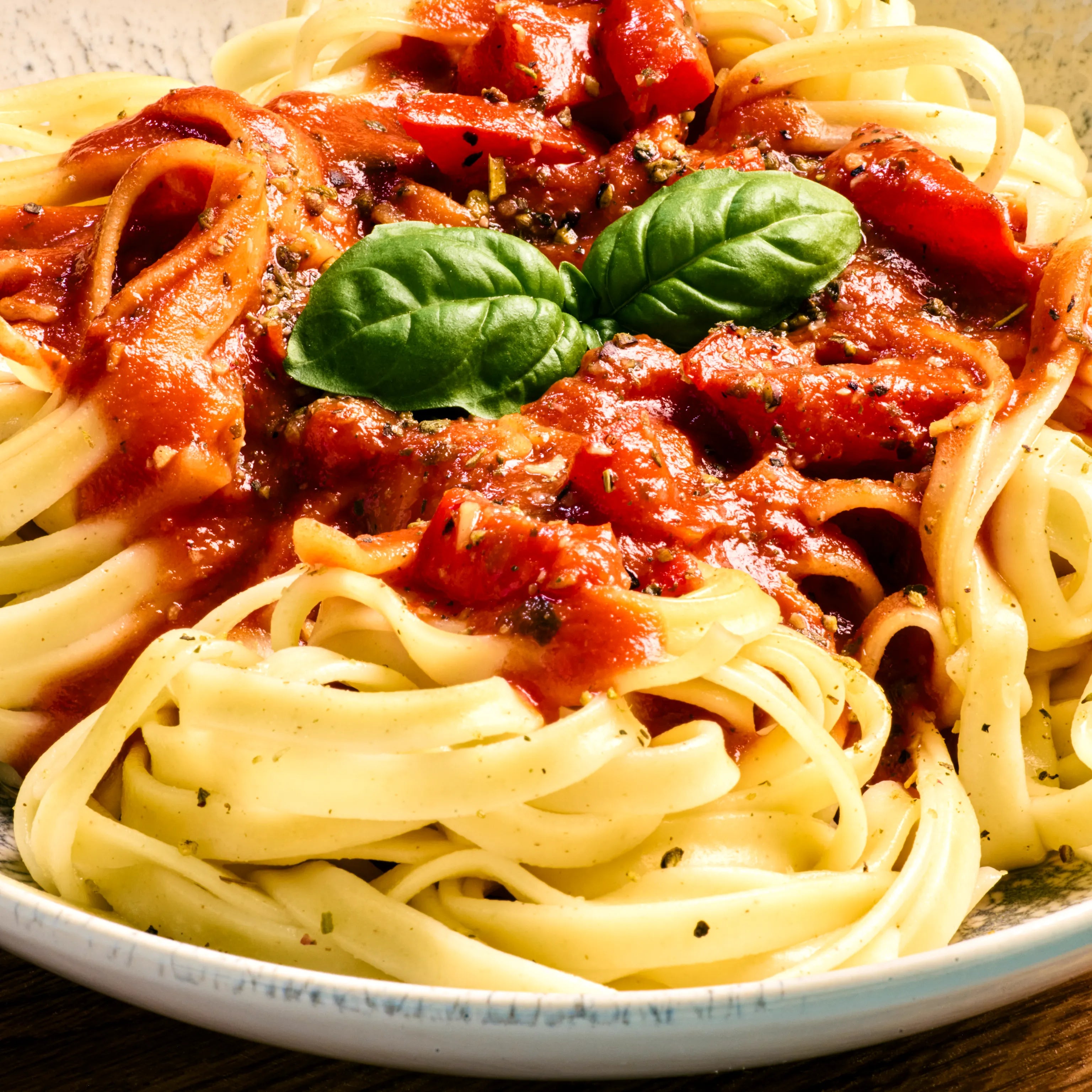 Bandnudeln mit Tomatensauce, Kräutern und frischem Basilikum auf einem Teller, appetitlich angerichtet