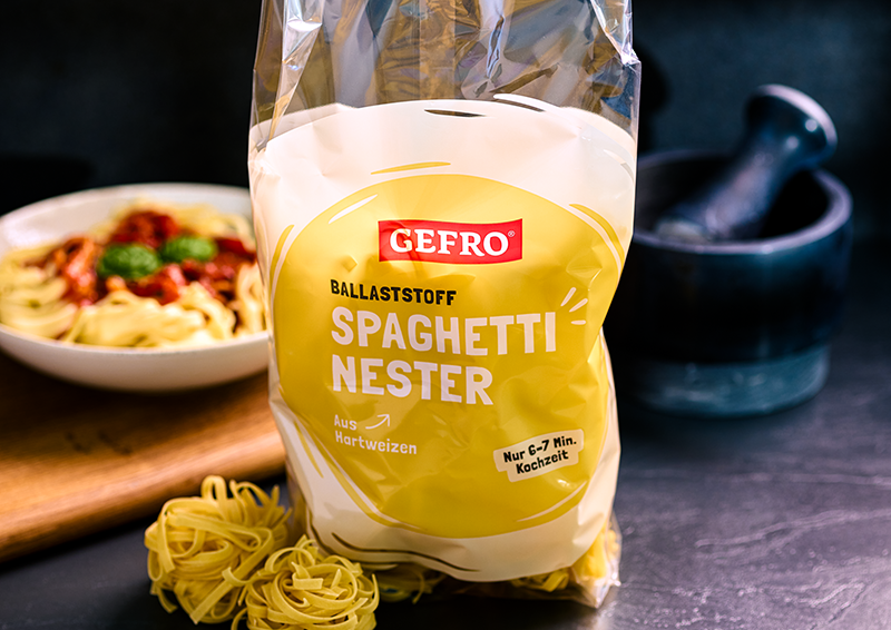 Verpackung von Gefro Spaghetti Nestern aus Hartweizen, davor rohe Nester, im Hintergrund ein Teller Pasta und Mörser