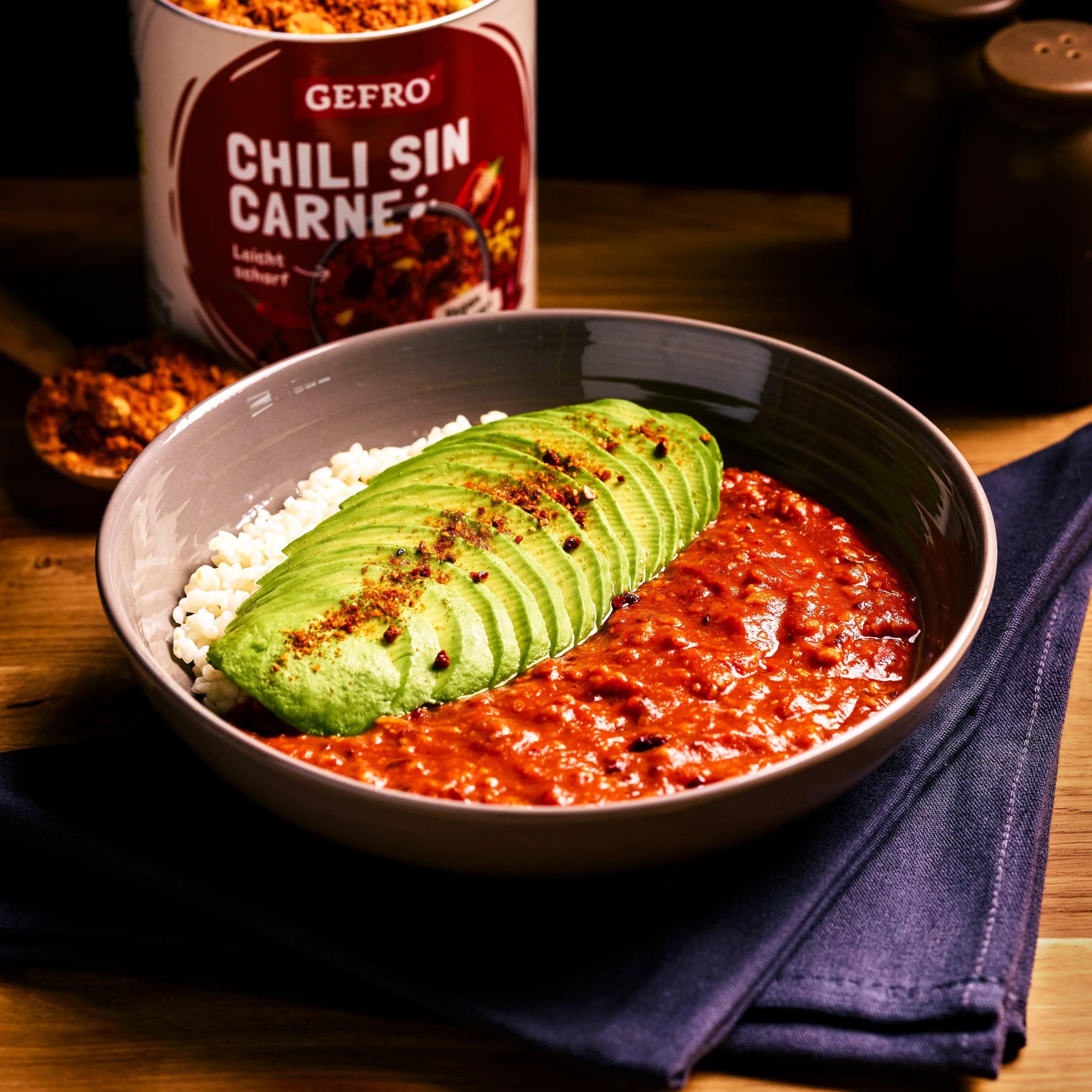 Schale mit Chili sin Carne, Reis und Avocadoscheiben, daneben Gewürzdose von GEFRO auf einem Holztisch.