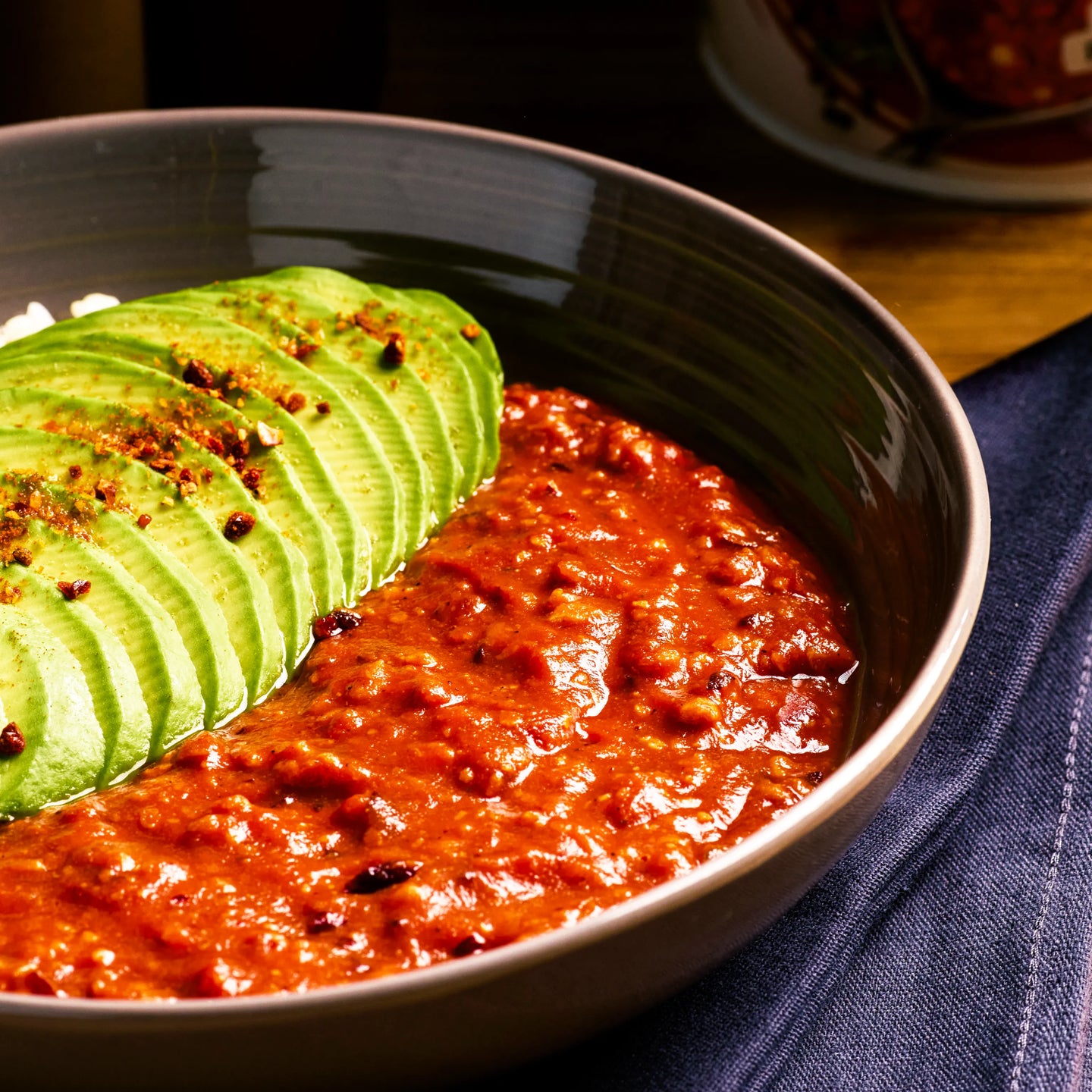 Schwarze Schale mit rotem Eintopf und fein geschnittener Avocado, serviert als warme, herzhafte Mahlzeit.