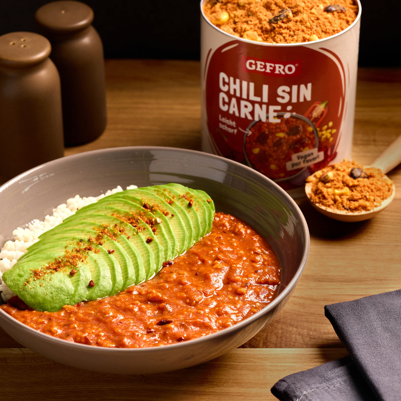 Schale mit Chili sin Carne, Reis und Avocadoscheiben, daneben Gewürzmischung von Gefro auf Holztisch präsentiert