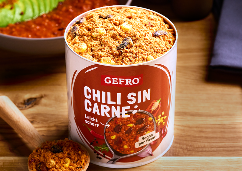 Dose GEFRO Chili sin Carne auf Holztisch, geöffnet mit Gewürzmischung, daneben ein Löffel mit Inhalt