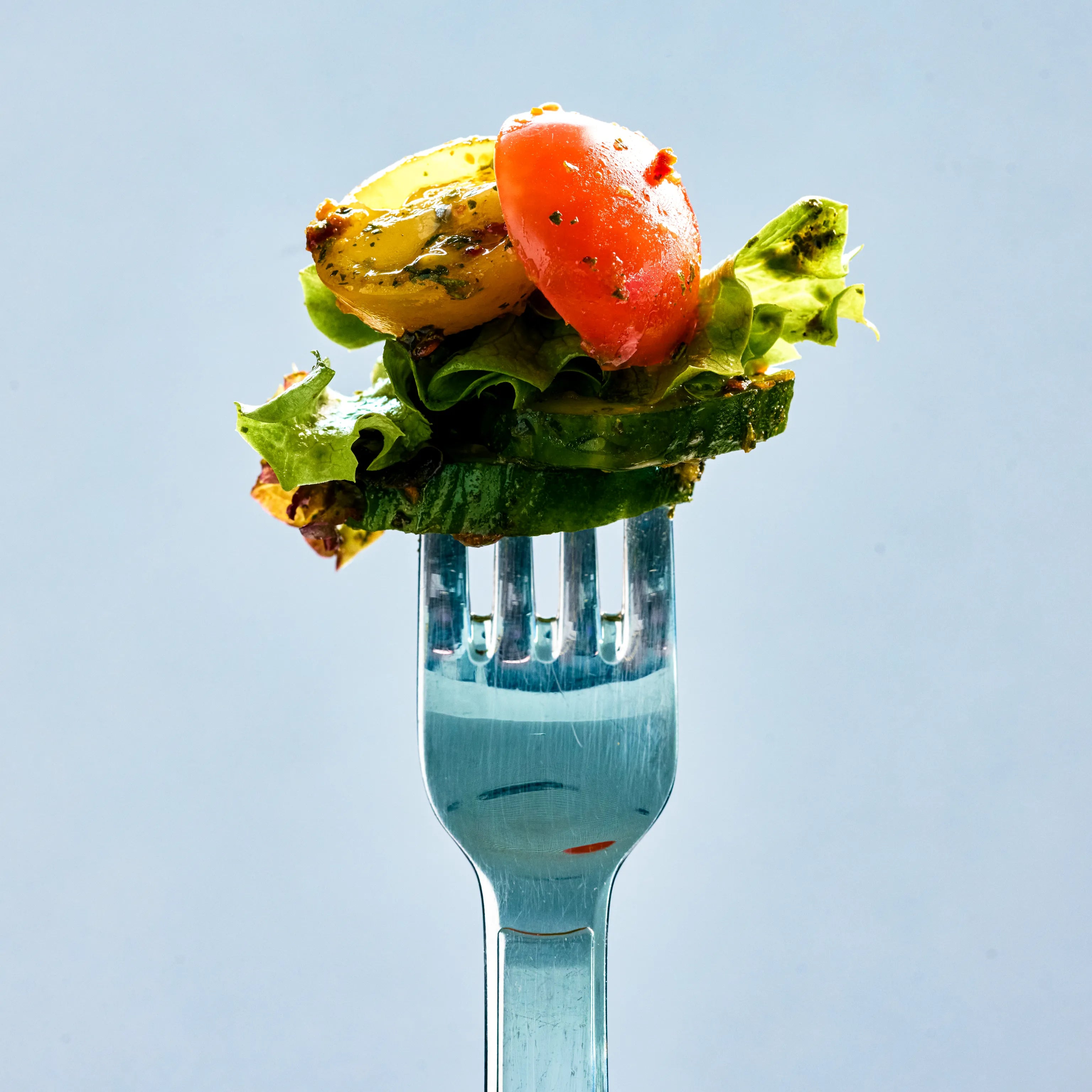 Gabel mit frischem Salat aus Gurke, Blattsalat und Tomatenstücken vor hellem Hintergrund, als leichte Mahlzeit präsentiert