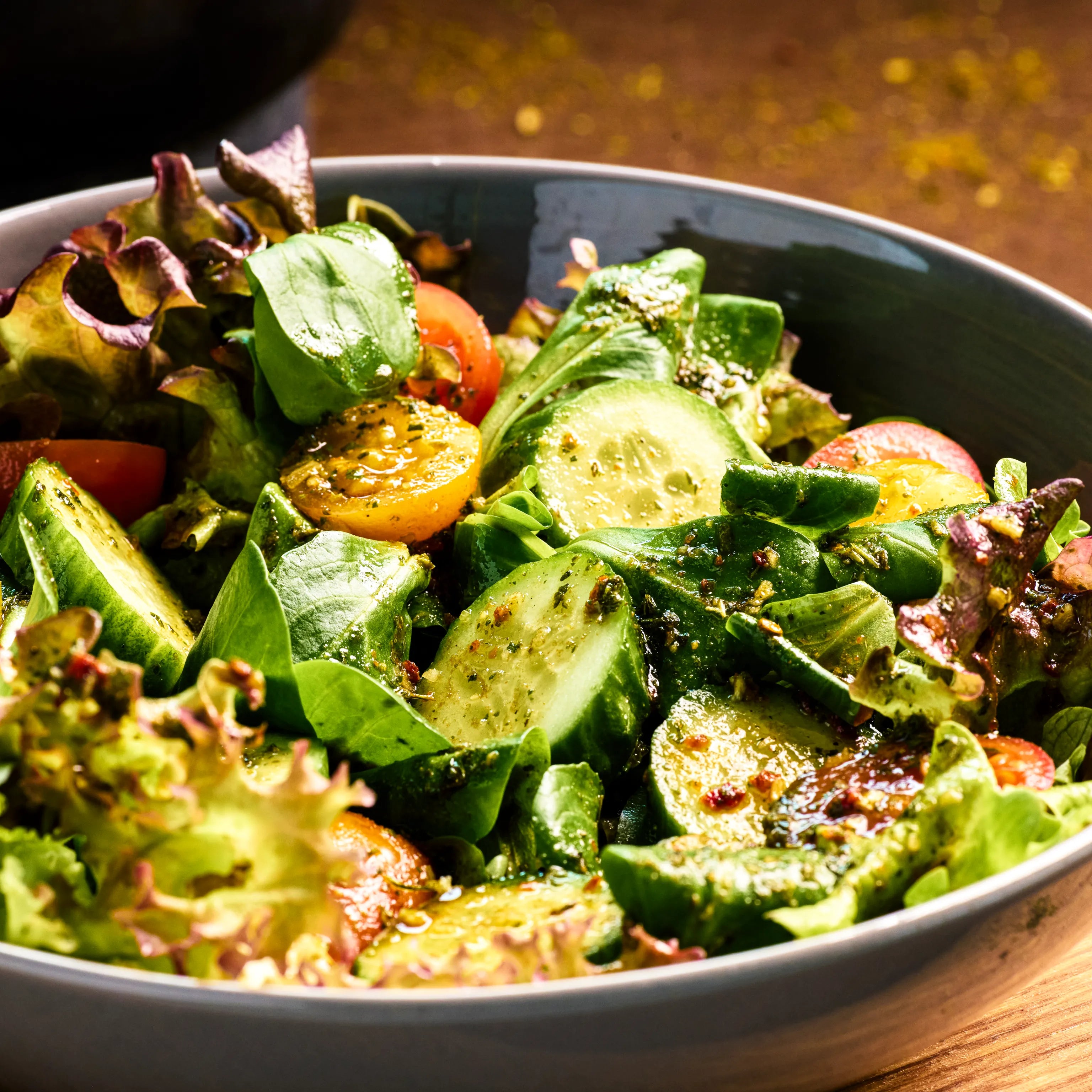 Schüssel mit frischem gemischtem Salat aus Gurke, Blattsalat, Tomaten und Kräuterdressing in Nahaufnahme