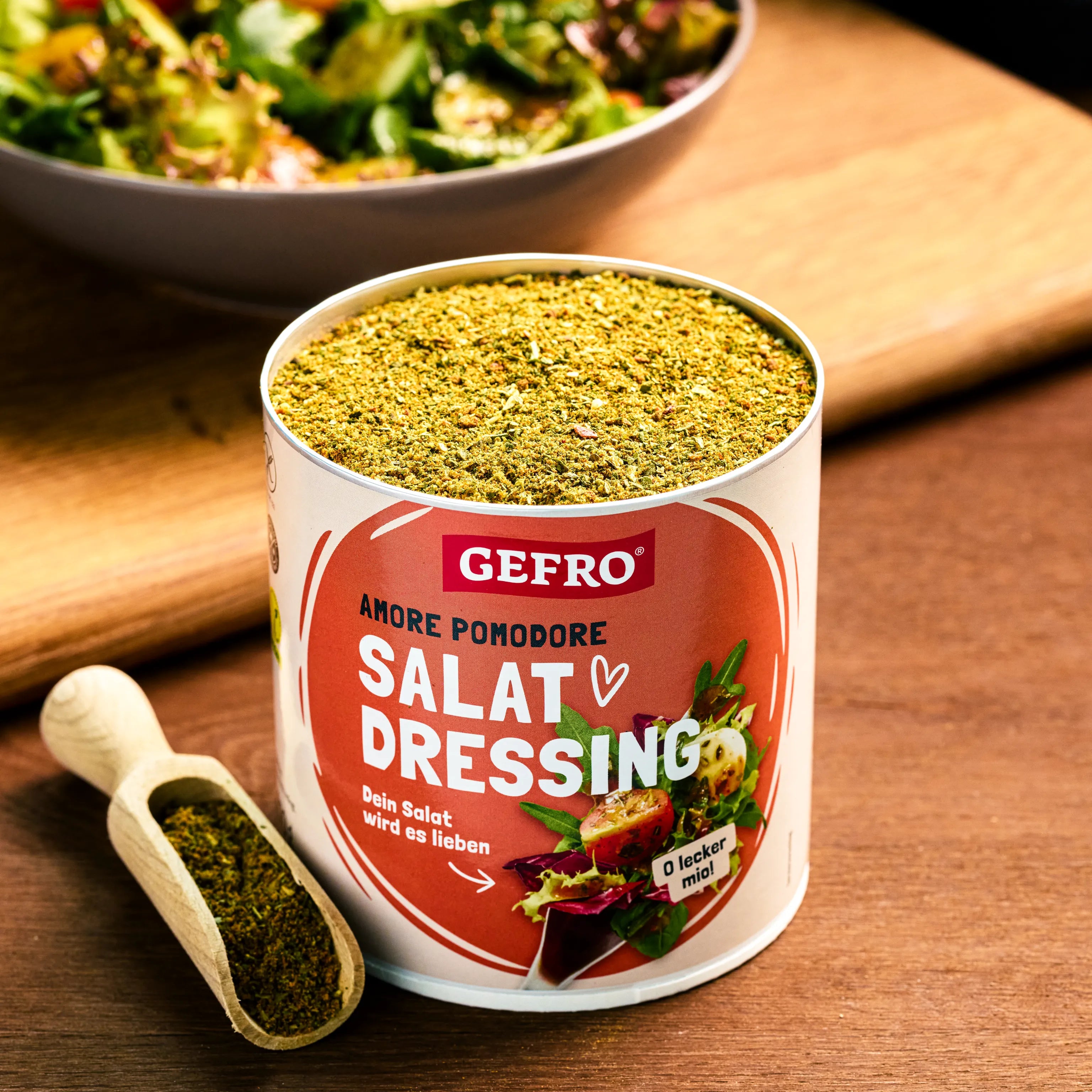 Dose mit GEFRO Salat-Dressing-Gewürz und Holzschaufel auf Tisch, dahinter eine Schüssel mit grünem Salat