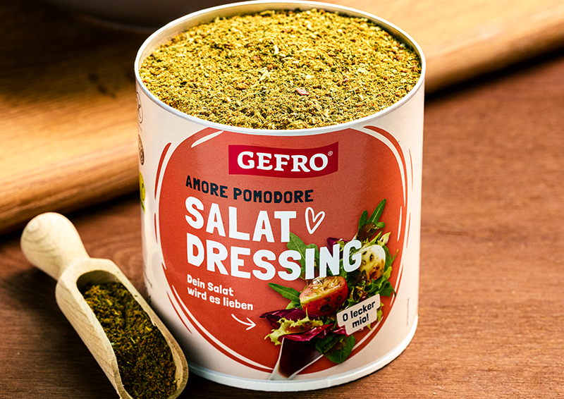 Dose GEFRO Amore Pomodore Salat Dressing mit Gewürzmischung, daneben ein Holzlöffel auf Holztisch