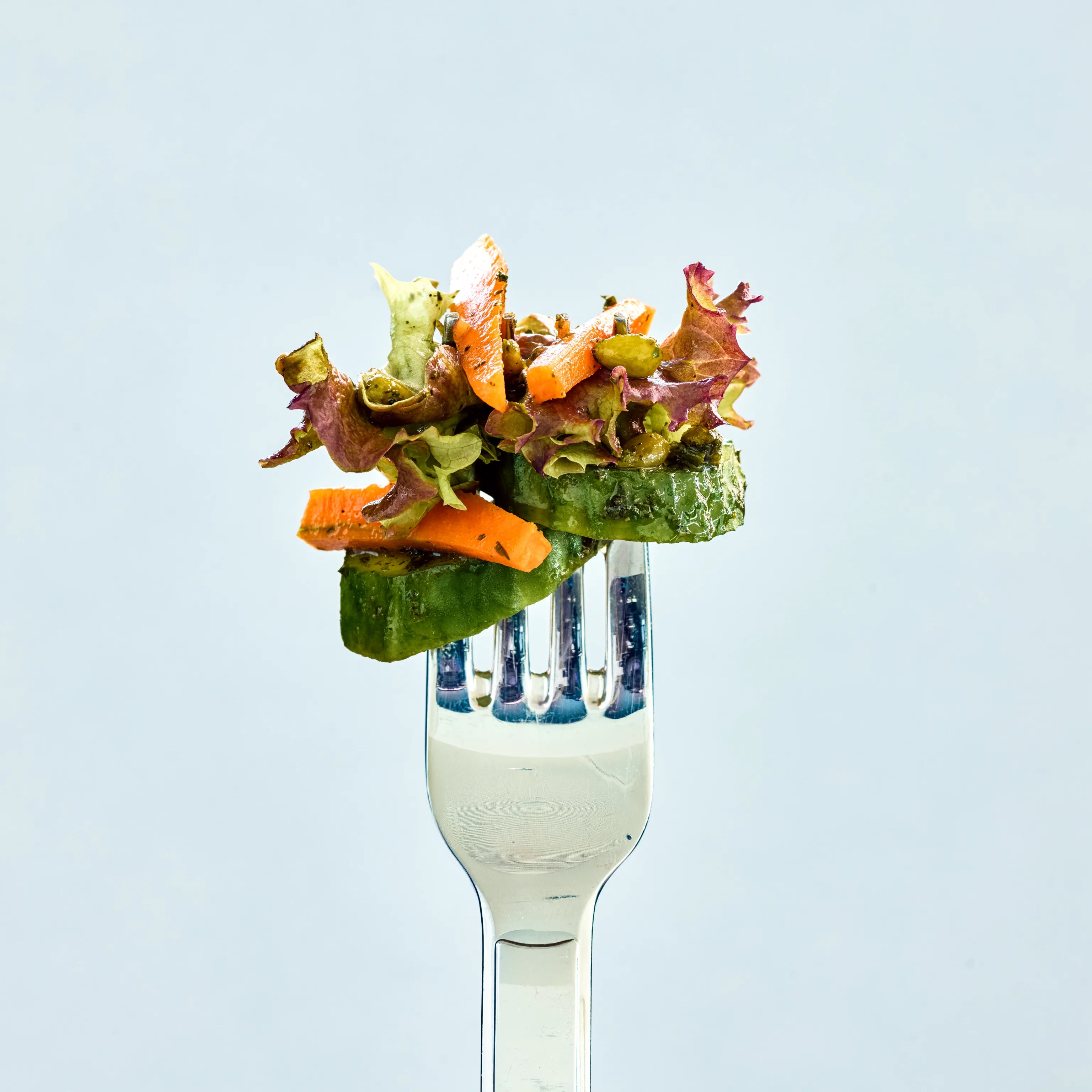 Gabel mit kleinem gemischtem Salat aus Gurke, Karotte und Blattsalat vor hellem Hintergrund, appetitlich angerichtet