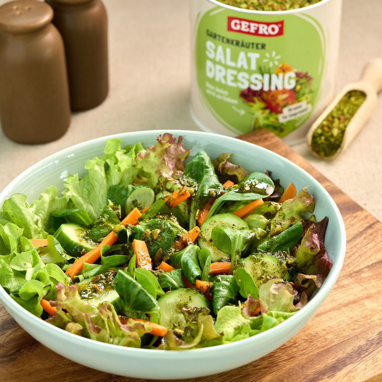 Schüssel mit frischem Blattsalat, Gurke und Karotten mit Kräuterdressing, daneben Packung Salat-Dressing von Gefro