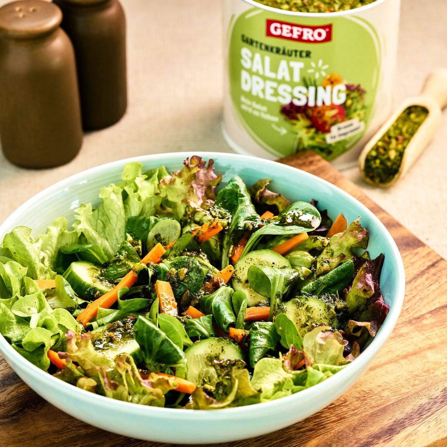 Schüssel mit gemischtem Blattsalat, Gurke und Karotten, daneben GEFRO Gartenkräuter Salat Dressing und Gewürze