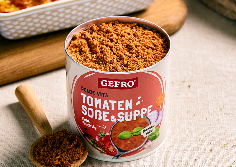 Dose mit Tomaten Soße & Suppe Pulver von Gefro auf Tisch, daneben ein Holzlöffel mit Gewürzmischung