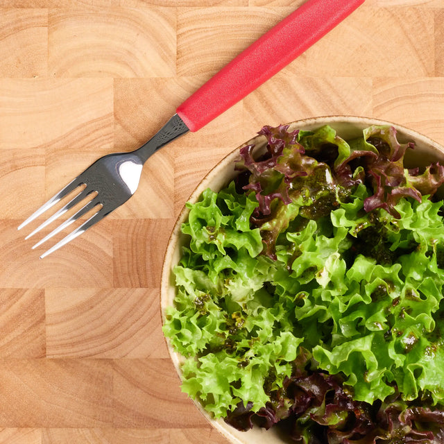 Salatschüssel mit grünem und rotem Blattsalat auf Holzbrett, daneben eine Gabel mit rotem Griff.