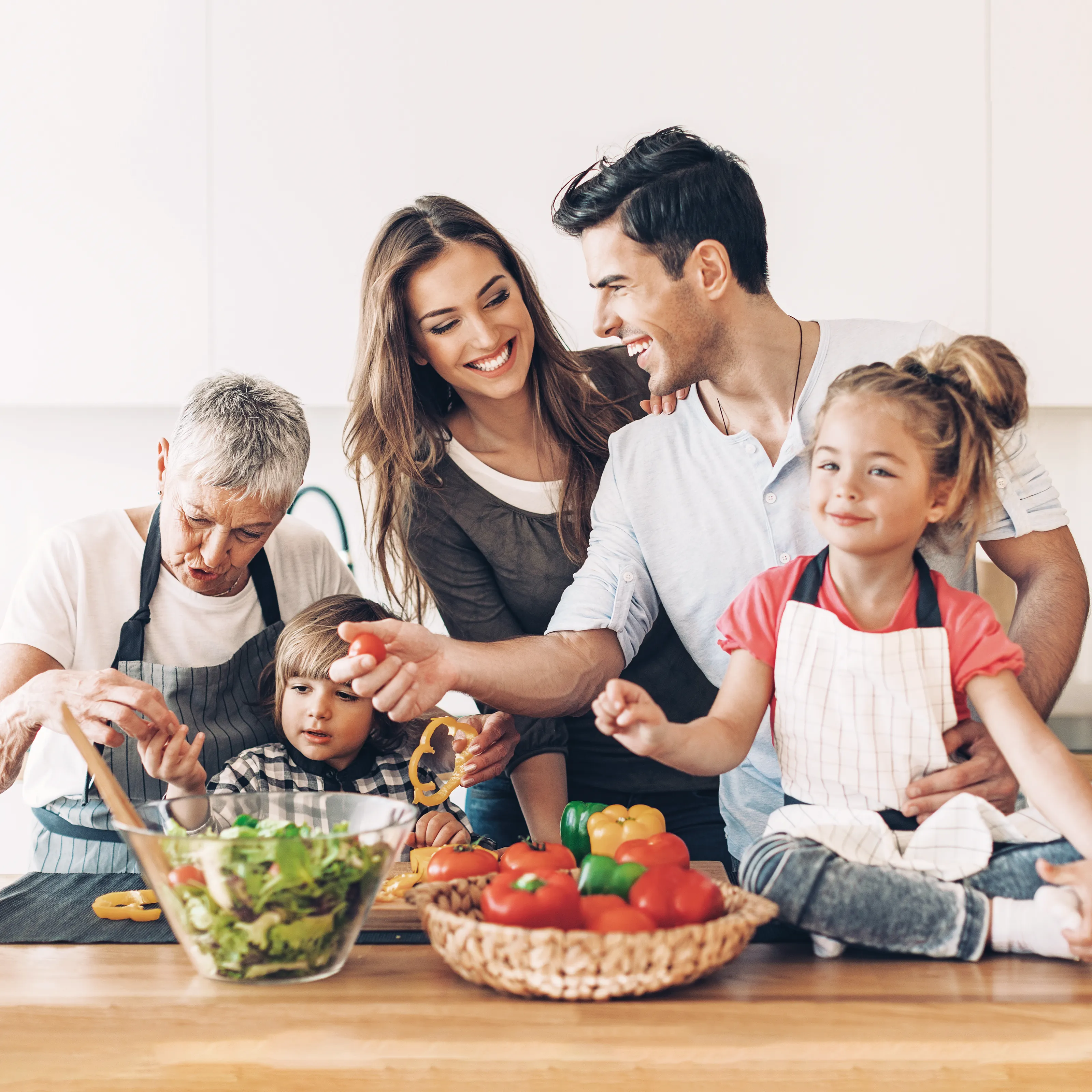 Familie mit Großmutter und Kindern bereitet gemeinsam in der Küche frischen Salat und Gemüse zu.