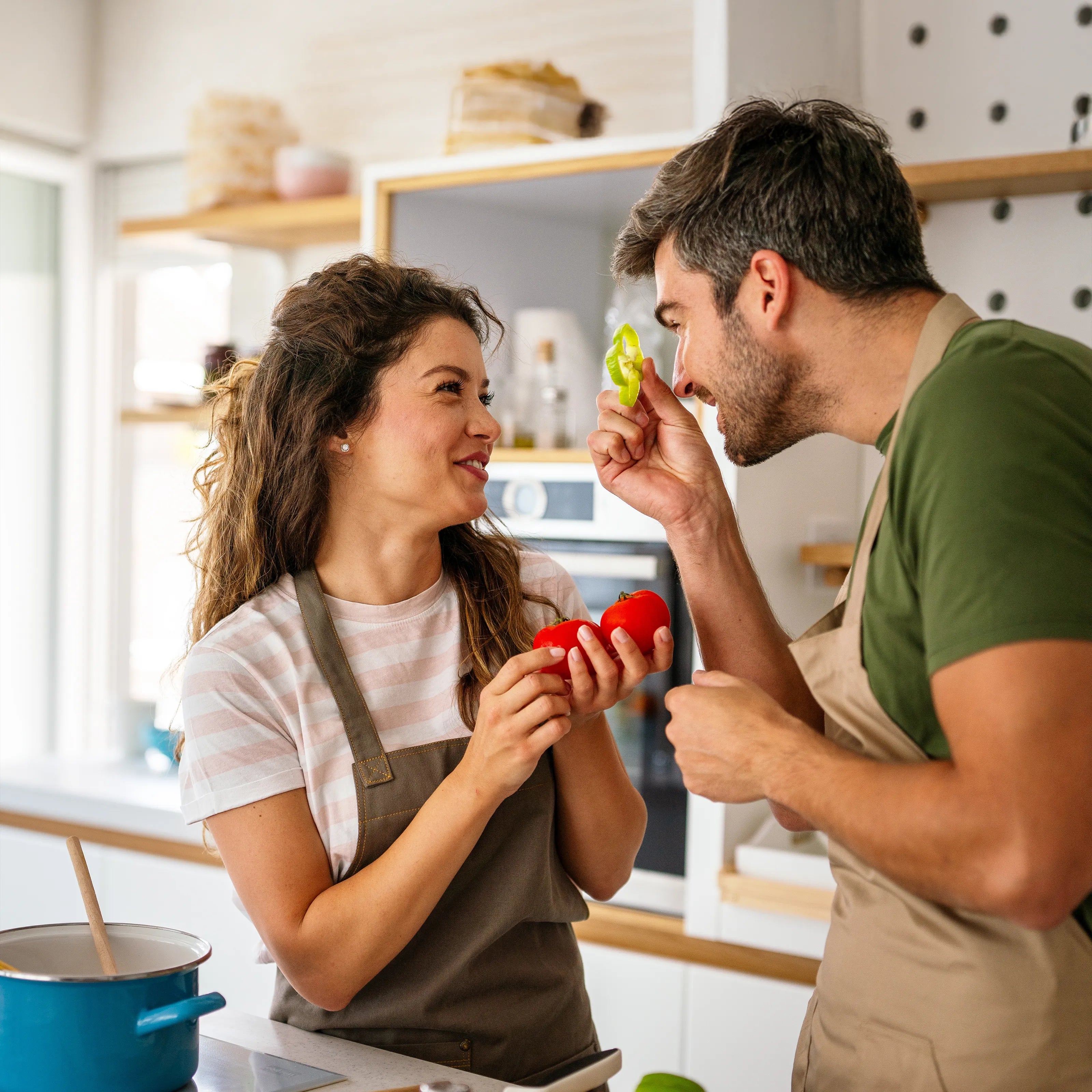 Zwei Personen mit Schürzen kochen in der Küche, halten Tomaten und Paprika und prüfen gemeinsam frische Zutaten.