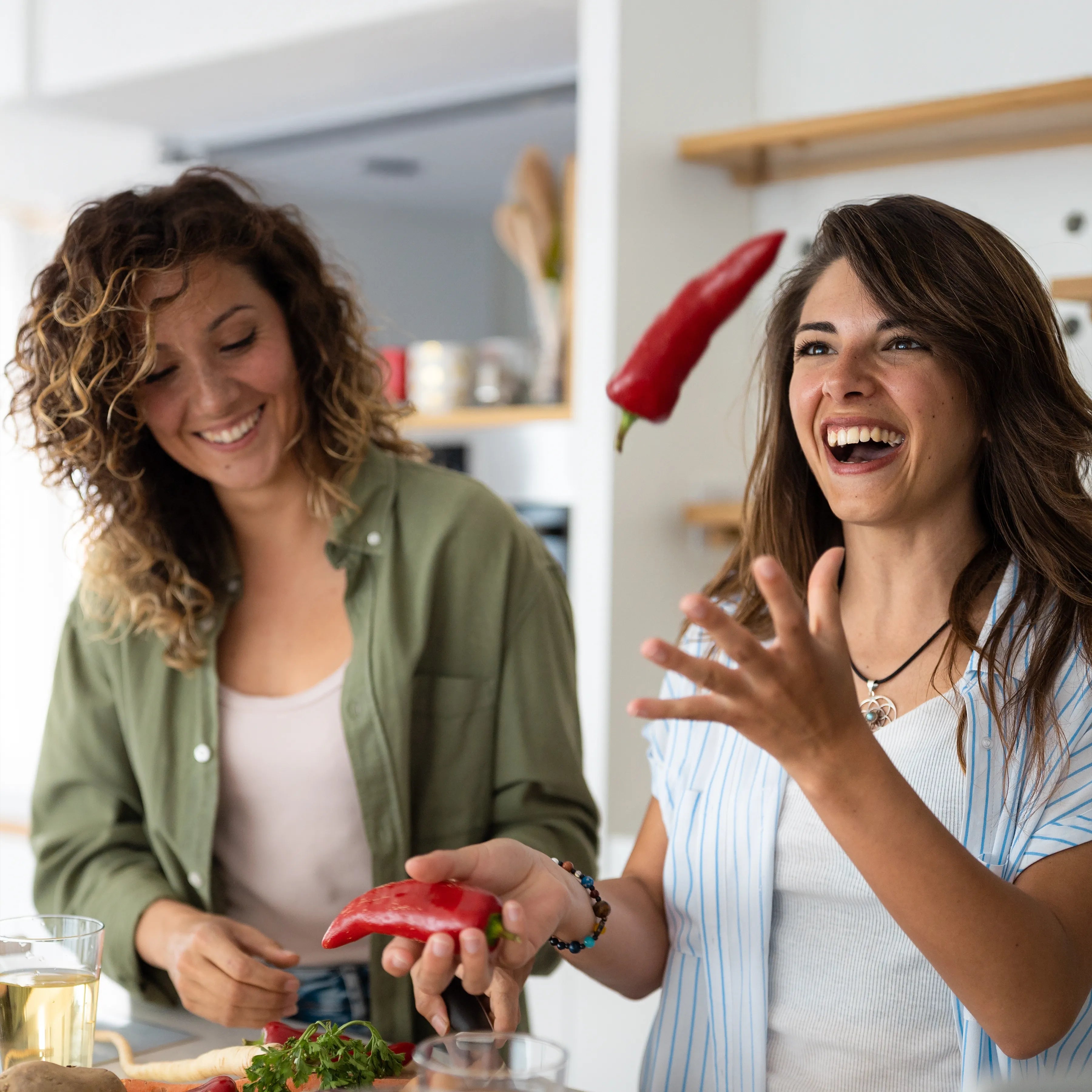 Zwei lachende Frauen in der Küche mit roten Paprikaschoten beim Kochen und Vorbereiten von Lebensmitteln