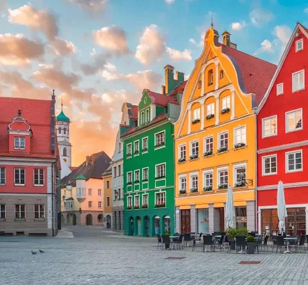 Bunter Marktplatz mit gelben, grünen und roten Häusern, Straßencafé und Kirchturm im warmen Abendlicht