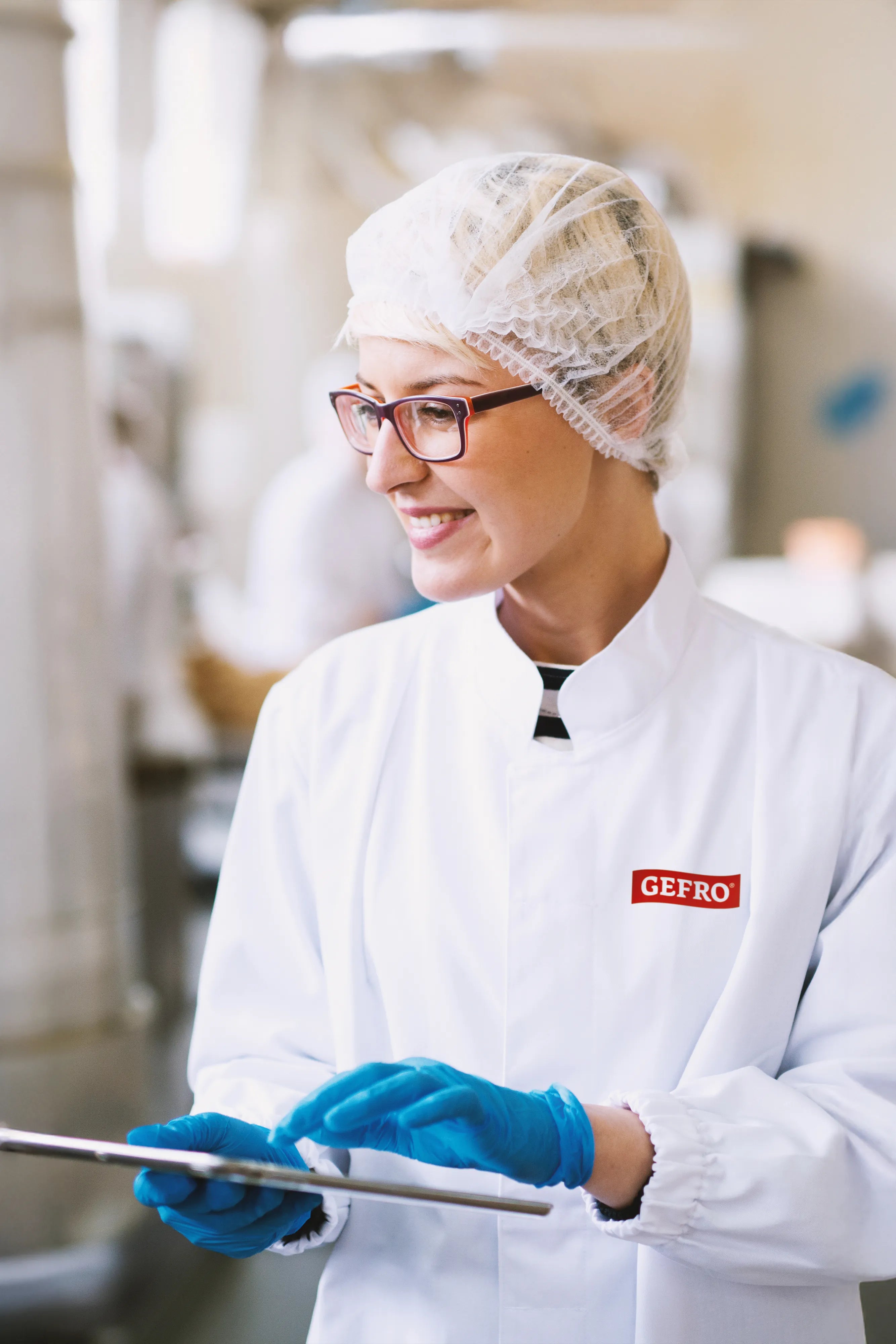 Mitarbeiterin in Schutzkleidung mit Haarnetz und Handschuhen prüft ein Tablet in der Lebensmittelproduktion