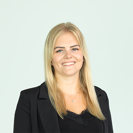 Porträt einer lächelnden blonden Frau in schwarzem Blazer vor hellem Hintergrund, geeignet für Team- oder Kontaktseite