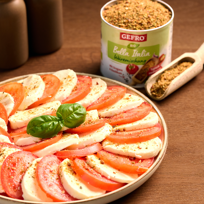 Tomaten-Mozzarella-Platte mit Basilikum und Gewürz, daneben Dose Bella Italia Bio Würzmischung und Holzschaufel