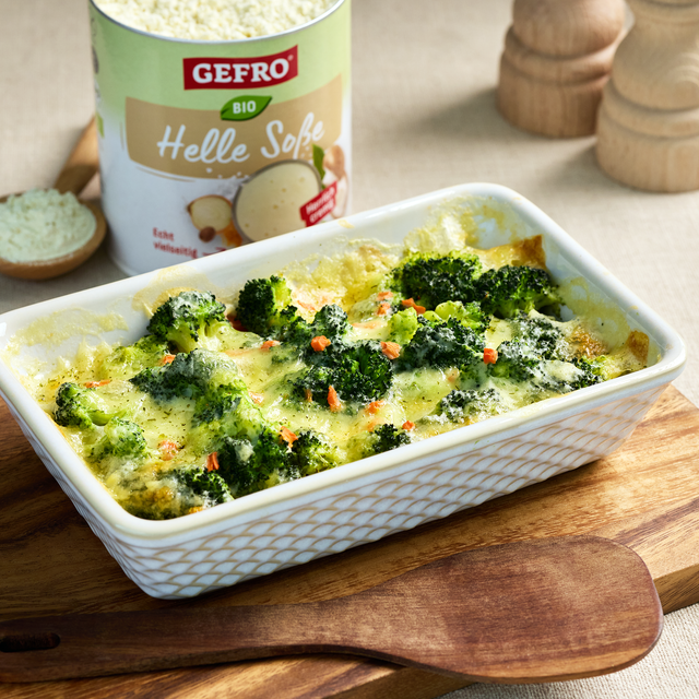 Brokkoli-Auflauf in weißer Form mit cremiger Sauce auf Holzbrett, daneben Dose GEFRO Bio Helle Soße.
