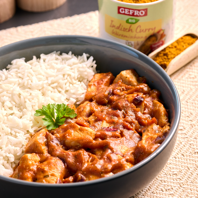 Schüssel mit weißem Reis und cremigem indischem Curry, daneben offene Gewürzdose und Löffel mit Currypulver