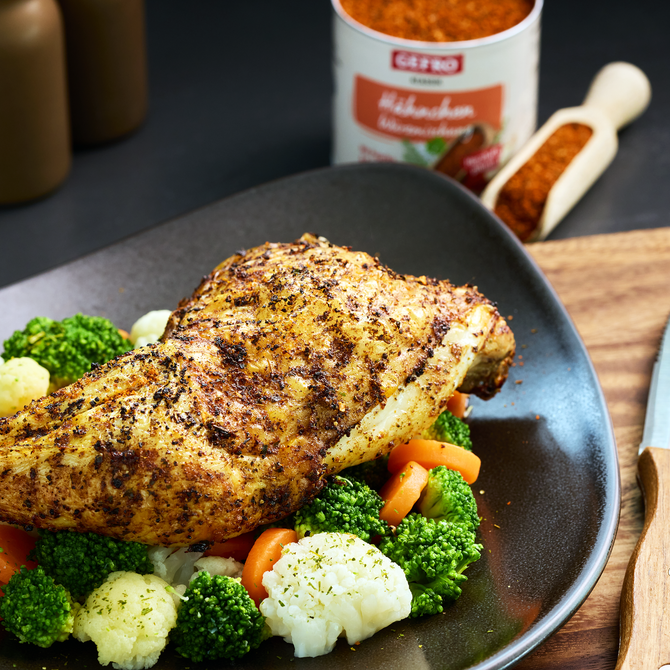 Gebratenes Hähnchen auf Brokkoli, Karotten und Blumenkohl, serviert auf schwarzem Teller mit Gewürz im Hintergrund