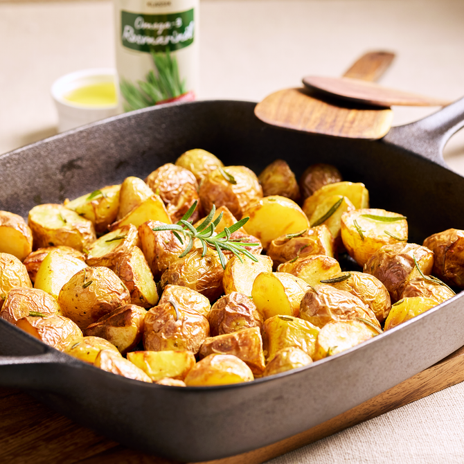Goldbraune Ofenkartoffeln mit Rosmarin in einer schwarzen Pfanne, servierfertig auf einem Holztisch angerichtet