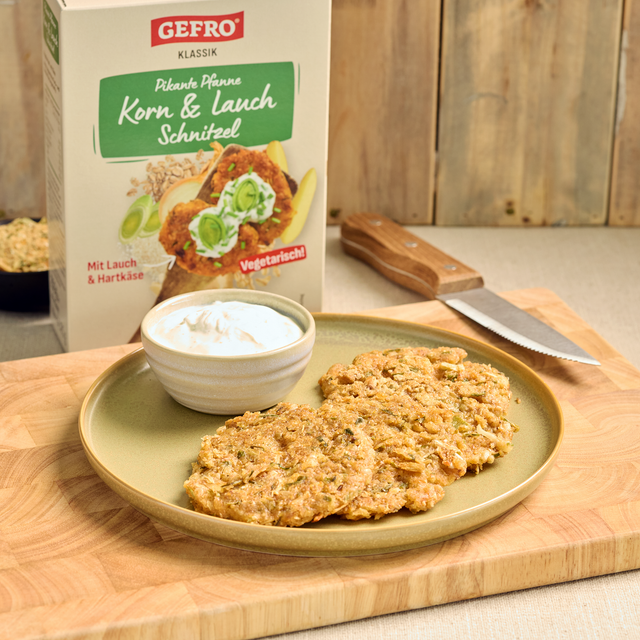 Teller mit Korn-Lauch-Schnitzeln und Dip vor GEFRÖ Verpackung auf Holzbrett, vegetarische Pfanne mit Lauch und Hartkäse