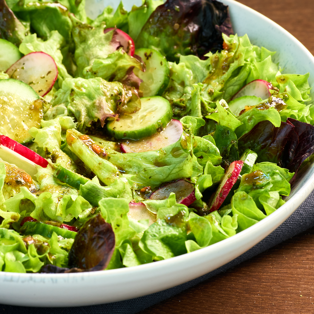 Schüssel mit frischem Blattsalat, Gurken- und Radieschenscheiben, angemacht mit grünem Dressing.