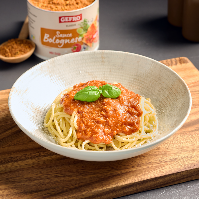 Teller mit Spaghetti und Bolognese-Sauce, garniert mit Basilikum; im Hintergrund eine Dose Gefro Sauce Bolognese.