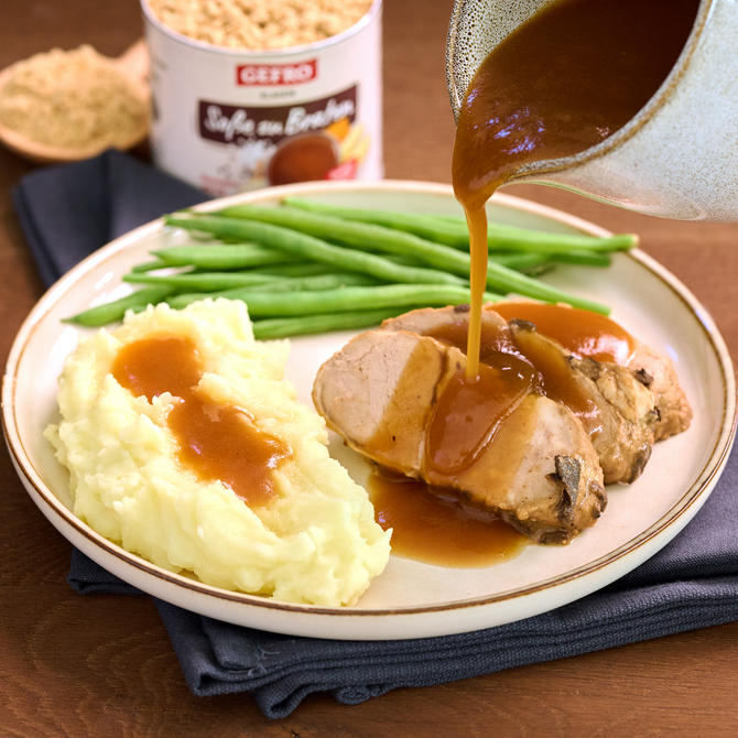 Kartoffelpüree, grüne Bohnen und Fleisch auf einem Teller, dazu braune Soße frisch aus einer Kanne eingegossen