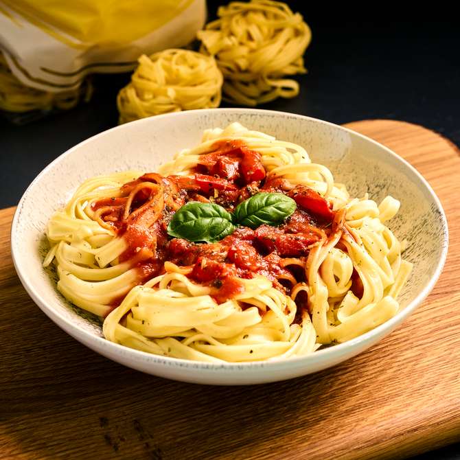 Teller mit Tagliatelle in Tomatensauce, garniert mit frischem Basilikum, auf einem Holzbrett serviert.