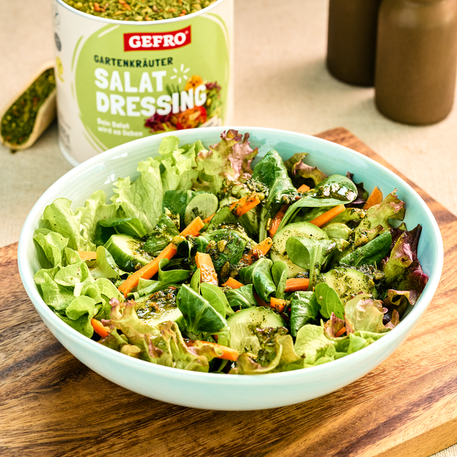 Schüssel mit grünem Salat, Gurke und Karotten, serviert mit Gartenkräuter-Salatdressing von Gefro im Hintergrund
