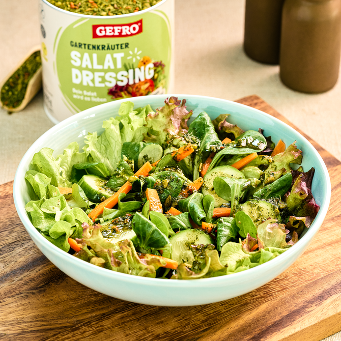 Schüssel mit grünem Salat, Gurke und Karotten, serviert mit Gartenkräuter-Salatdressing von Gefro im Hintergrund