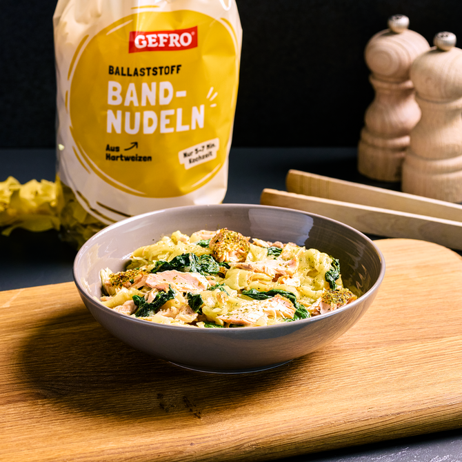 Schale mit Bandnudeln, Lachs und Spinat auf Holzbrett, daneben Packung GEFRO Ballaststoff-Bandnudeln