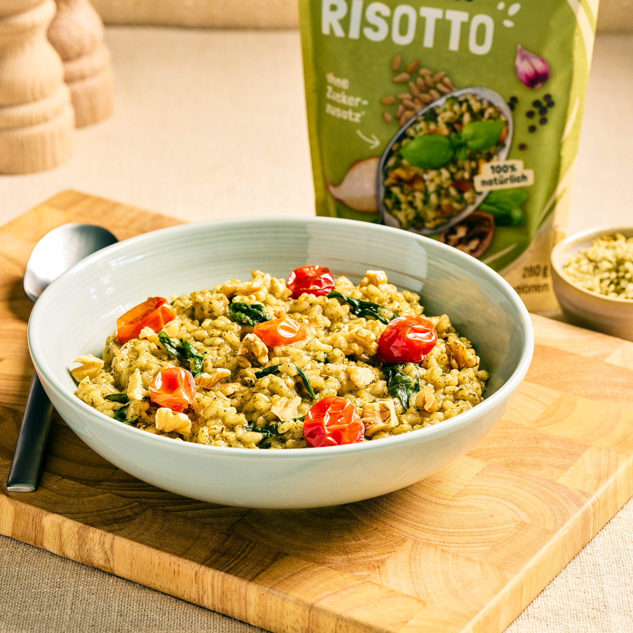 Schale mit grünem Risotto, garniert mit Cherrytomaten und Walnüssen, daneben die passende Produktverpackung.