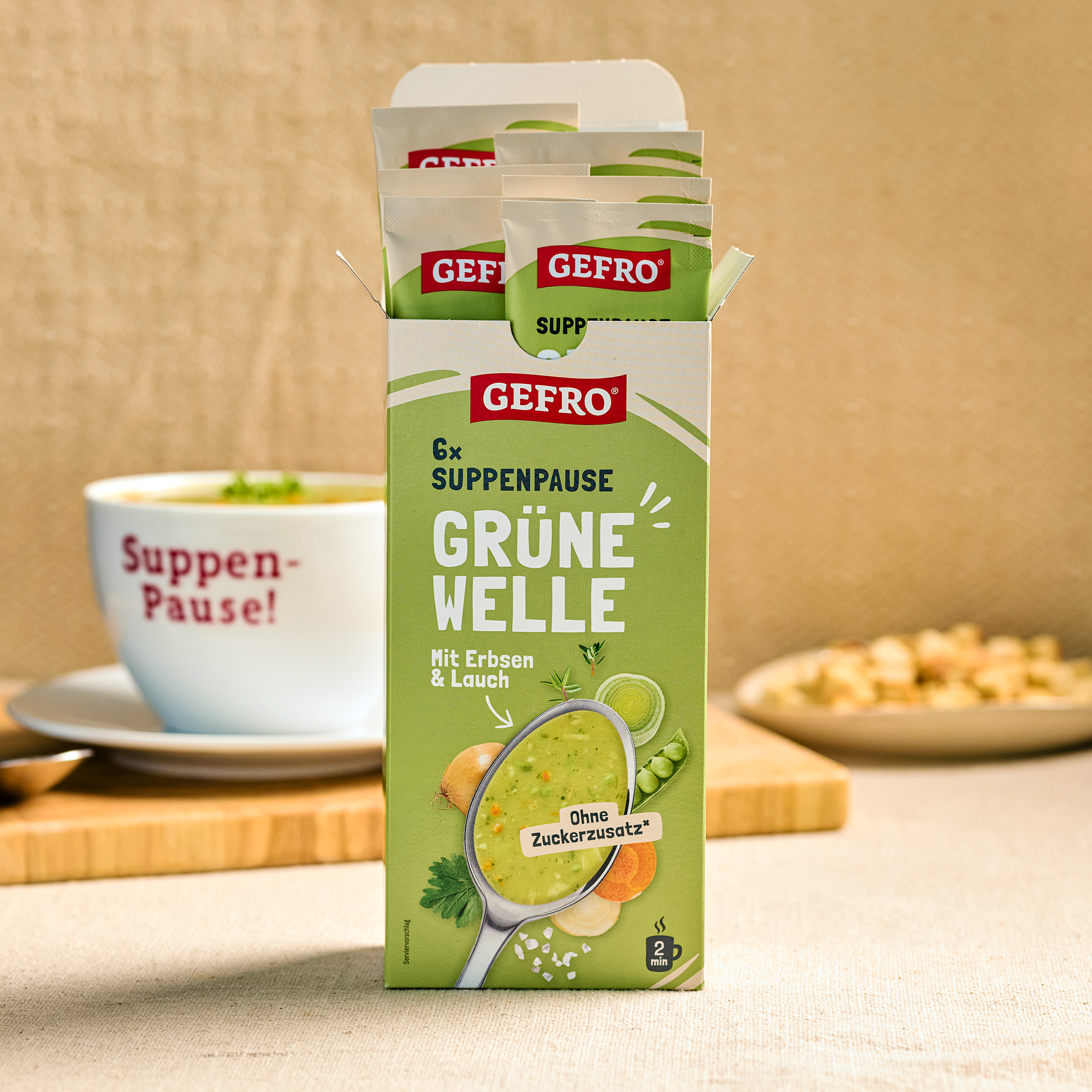 Offene Packung GEFRO Suppenpause Grüne Welle mit Erbsen und Lauch, Portionsbeutel vor einer Suppentasse.