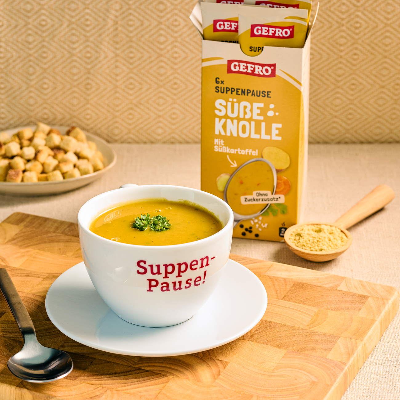 Schale mit gelber Süßkartoffelsuppe vor GEfro Suppenpause Süße Knolle Verpackung auf einem Holzbrett serviert