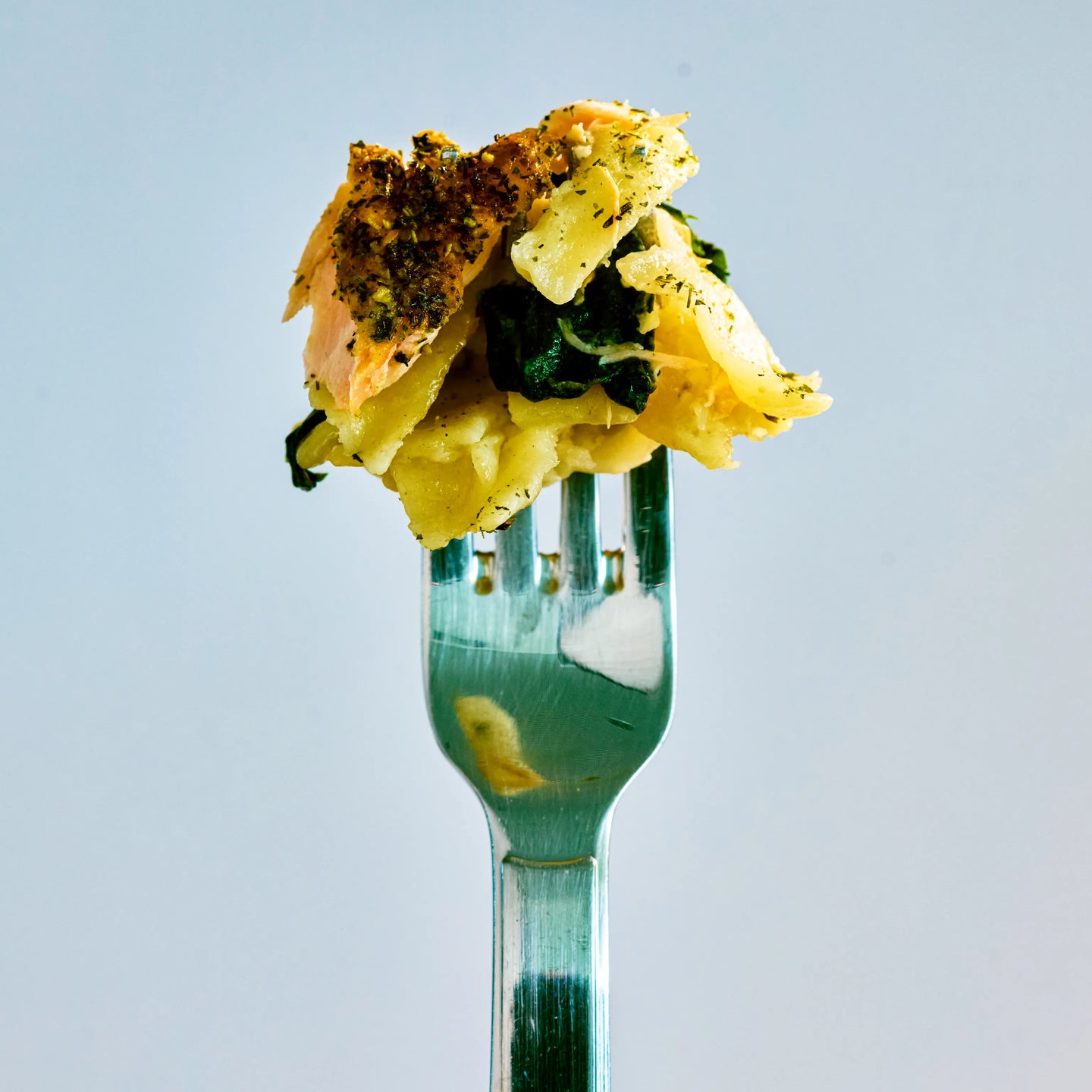 Gabel mit einer Portion Pasta, Lachs und Spinat vor hellem Hintergrund, als appetitliche Nahaufnahme serviert