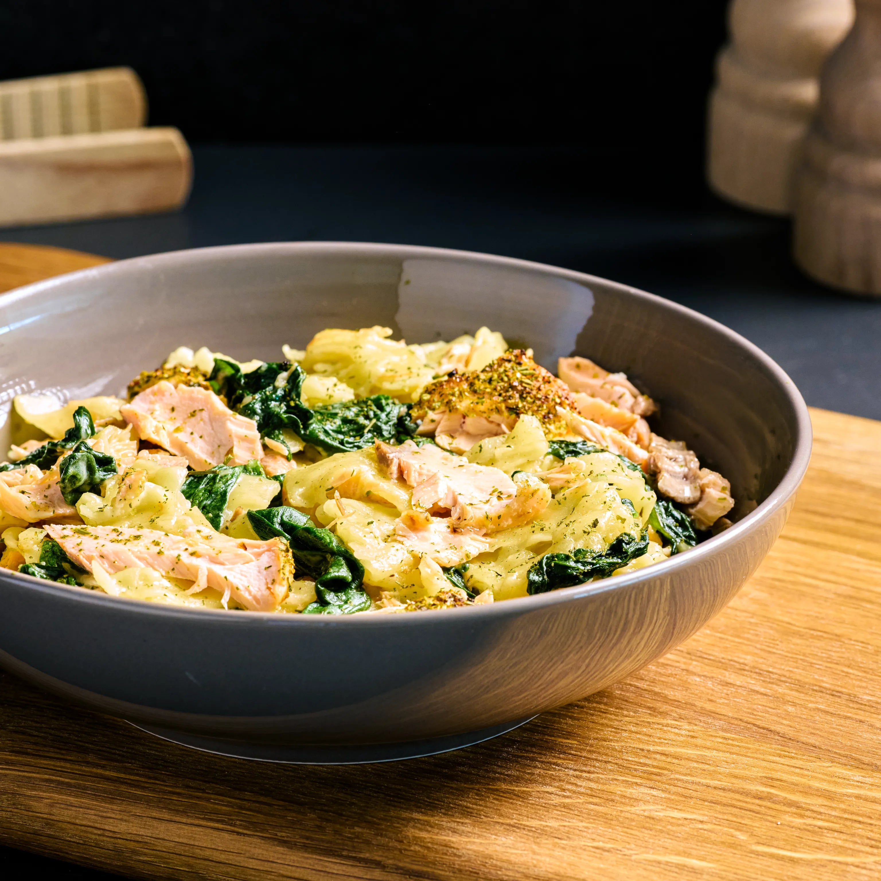 Schale mit Bandnudeln, Lachs und Spinat auf Holzbrett, serviert als warmes Hauptgericht in cremiger Sauce