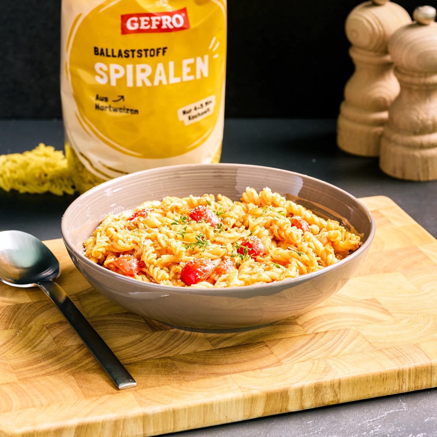 Schüssel mit Spiralnudeln in Tomatensauce auf Holzbrett, dahinter Verpackung von GEFRO Ballaststoff Spiralen