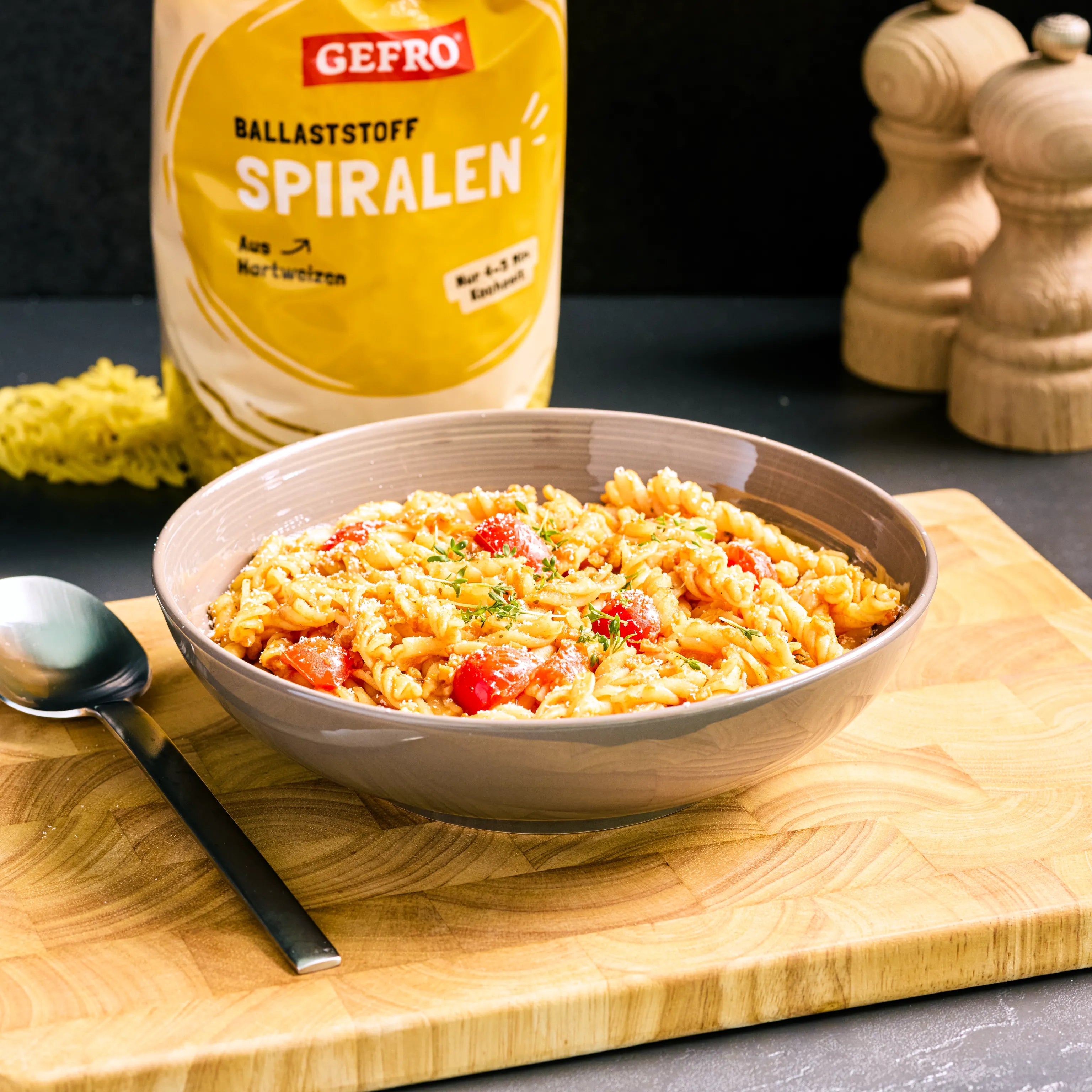 Schüssel mit Spiralnudeln in Tomatensauce auf Holzbrett, dahinter Verpackung von GEFRO Ballaststoff Spiralen