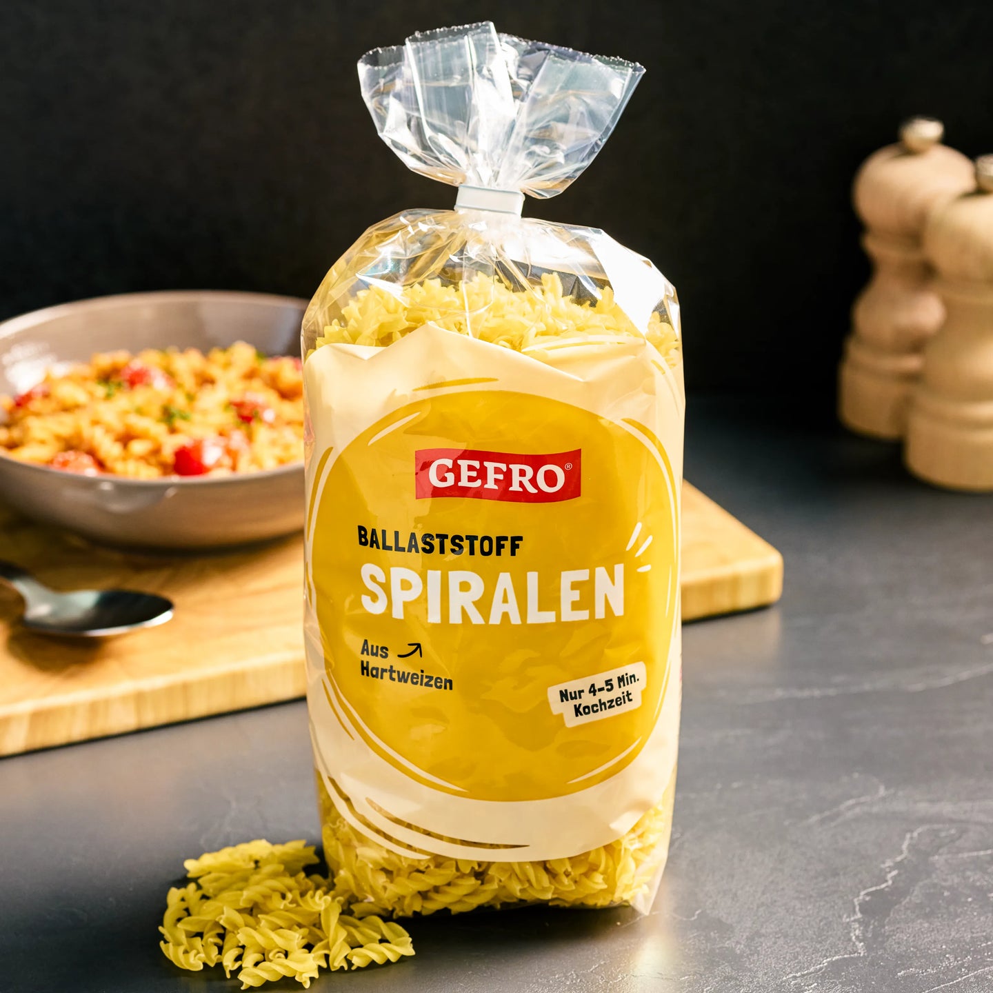 Packung GEFRO Ballaststoff Spiralen aus Hartweizen auf der Küchenplatte, davor einige Nudeln, Schüssel im Hintergrund