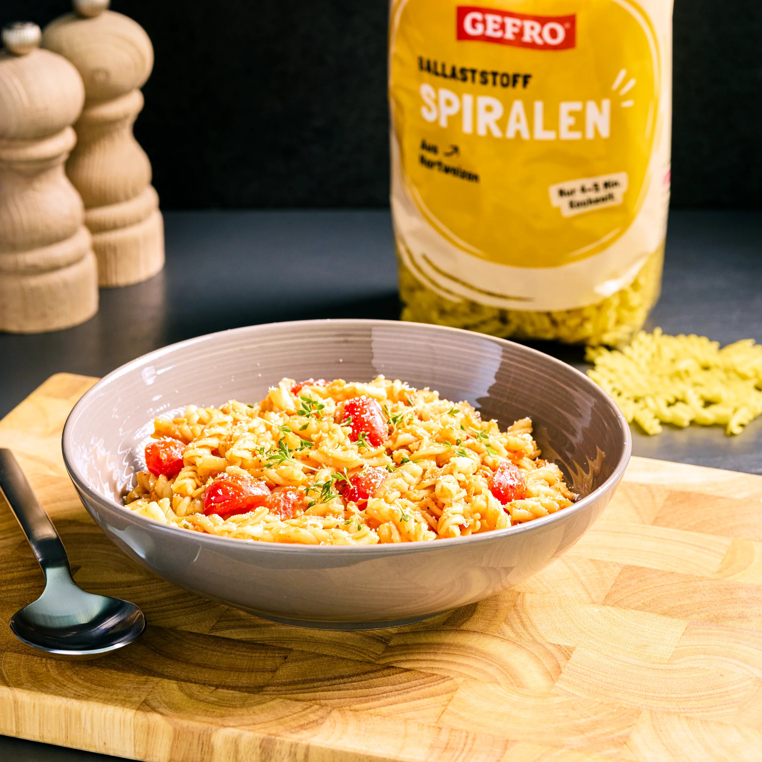 Schale mit Spiralnudeln, Cherrytomaten und Kräutern auf Holzbrett, dahinter eine Packung GEFRO Ballaststoff Spiralen