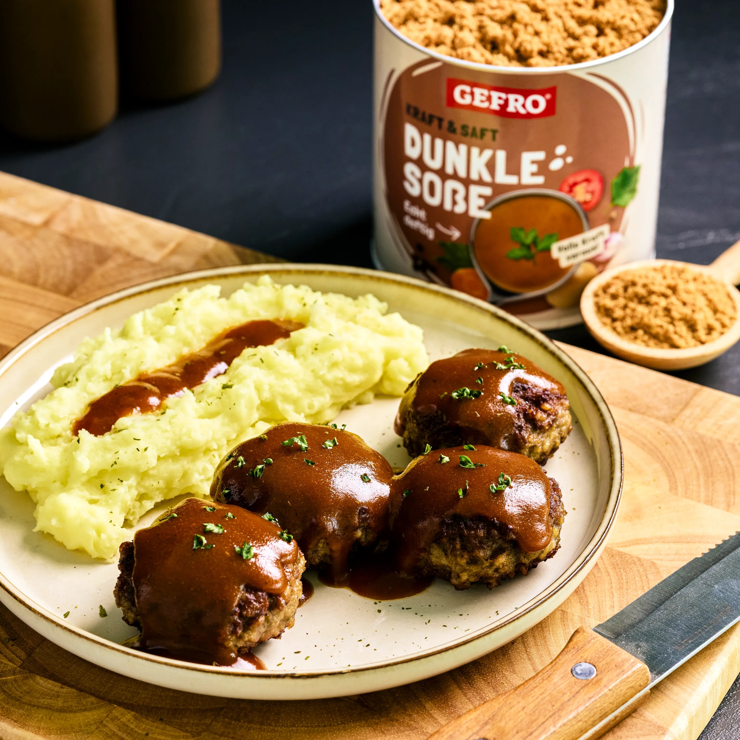 Teller mit Kartoffelpüree und vier Frikadellen mit dunkler Soße, daneben Gefro Dunkle Soße Pulverdose.